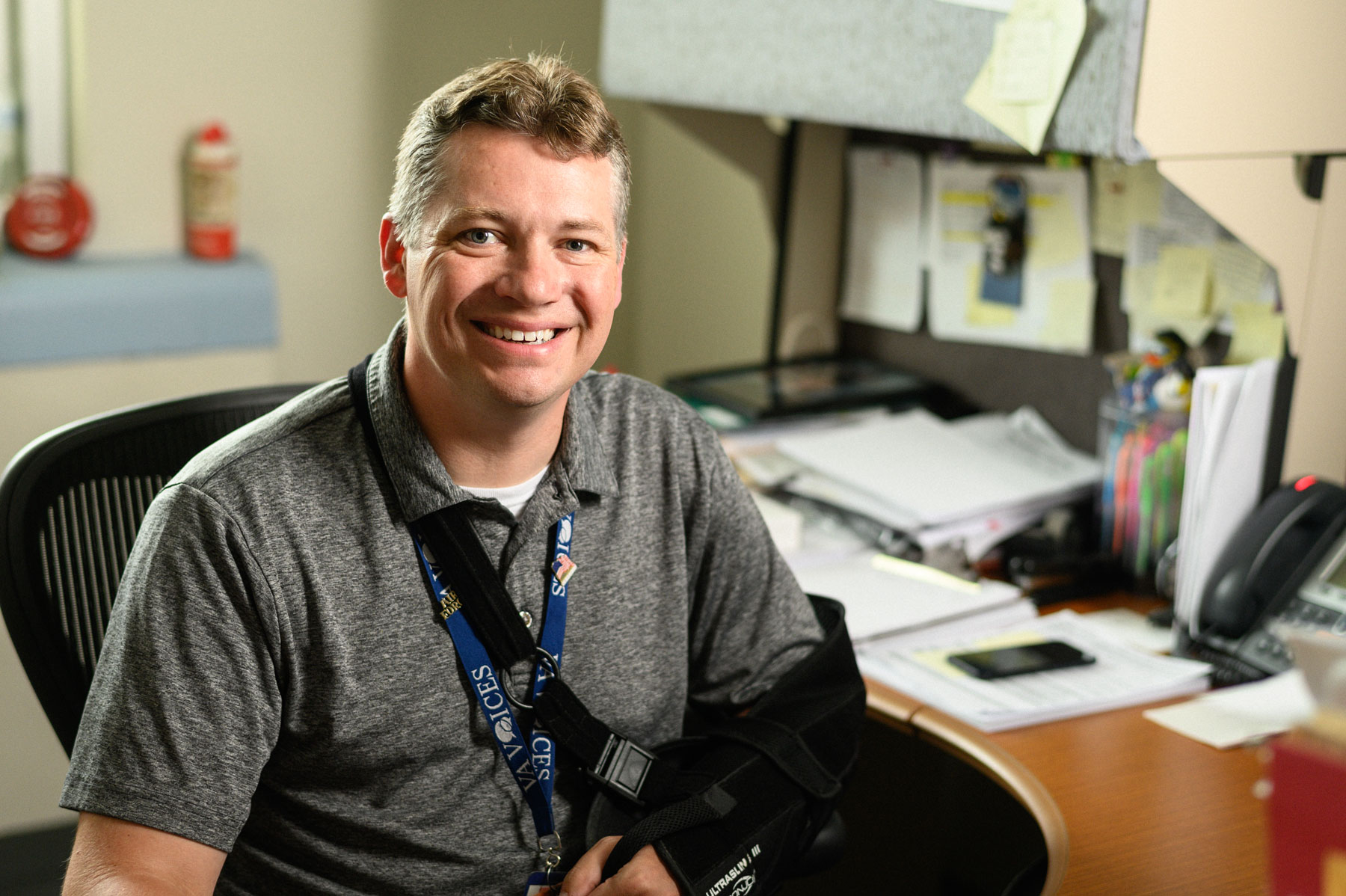 Leonard smiles from his desk with his arm in a sling.
