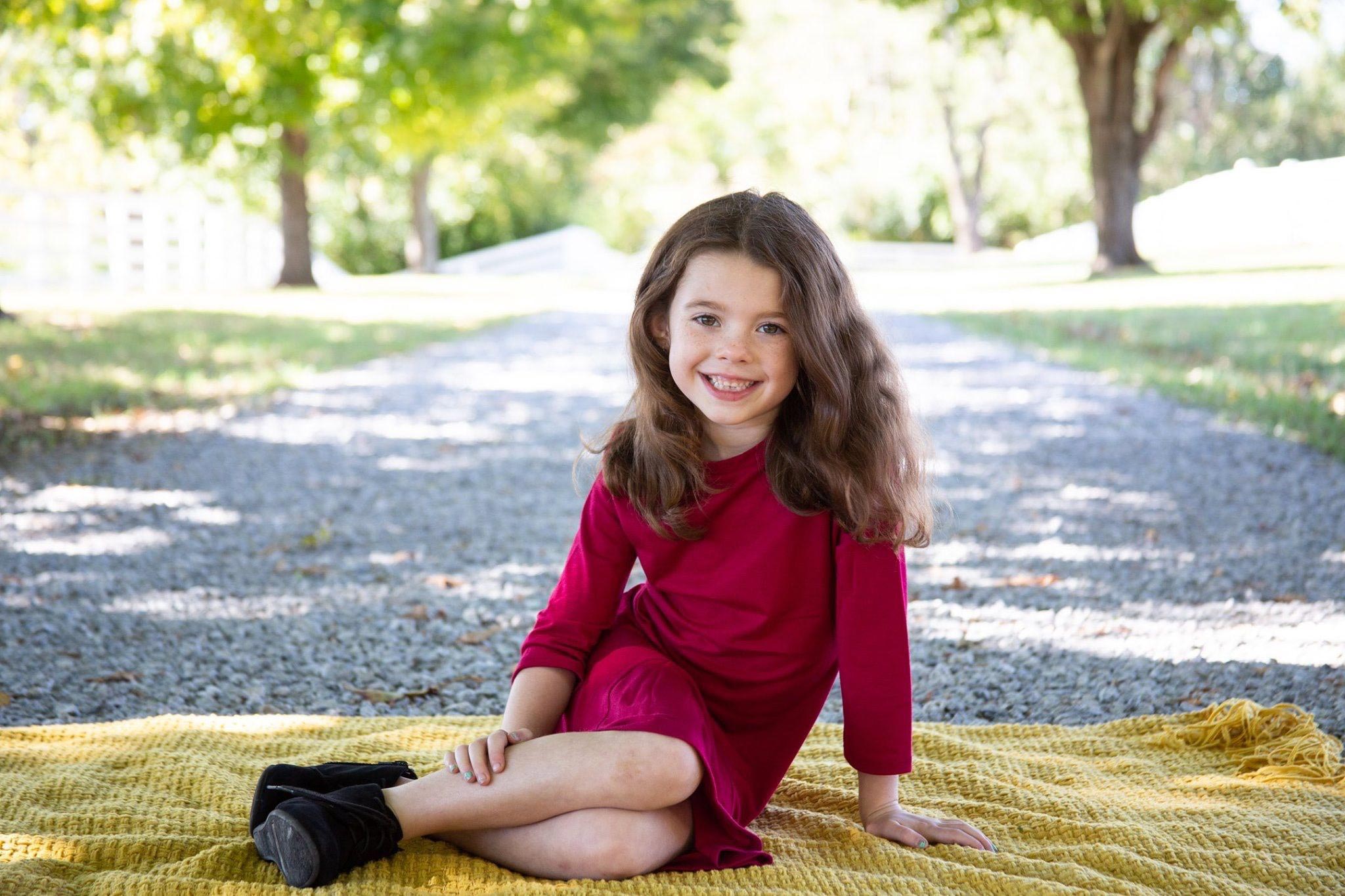 Izzy leans on one arm while sitting on a yellow blanket in her driveway and smiles.