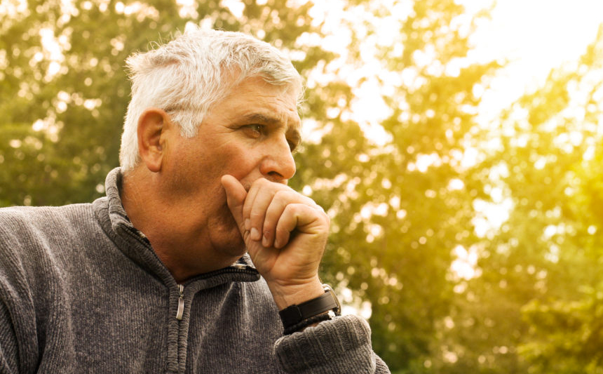 A senior man covers his mouth as he coughs.