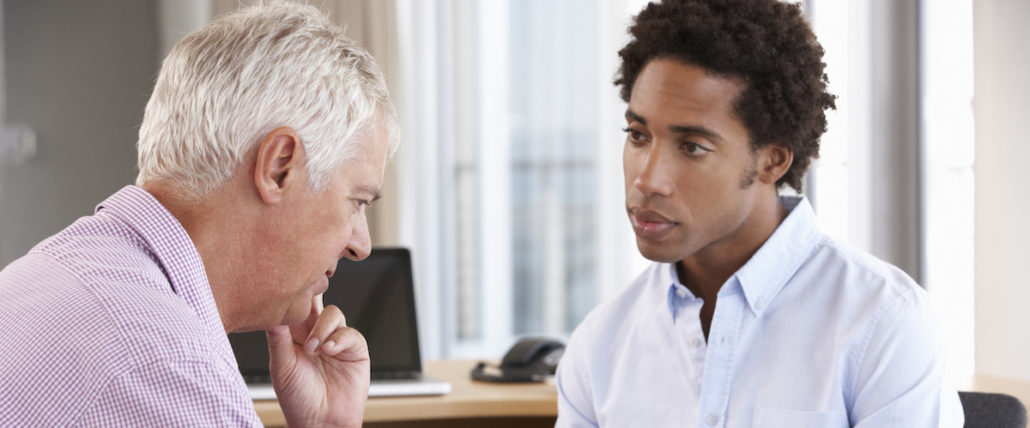 A senior man talks with a young man.