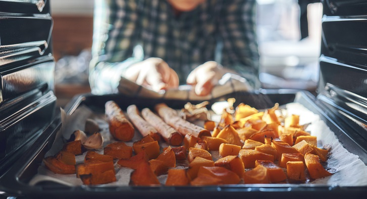 Man removes baking sheet of squash and carrots out of the oven.