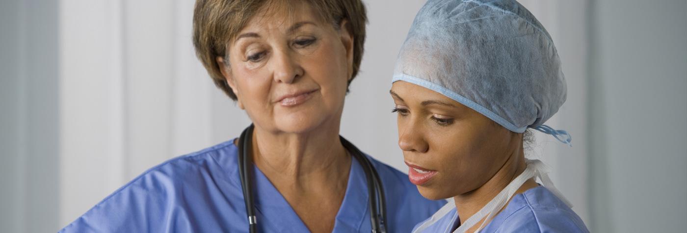 two female doctors wearing blue scrubs while reading and discussing a patient's chart