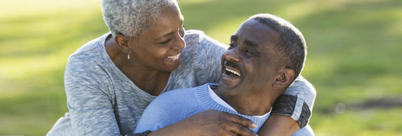 Middle aged African American man and woman sitting outdoors and laughing together.