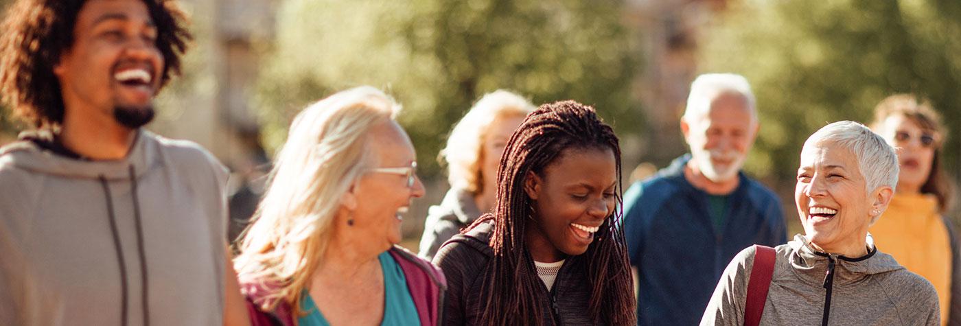 A group of adults of varying ages walks together outdoors while talking and laughing.