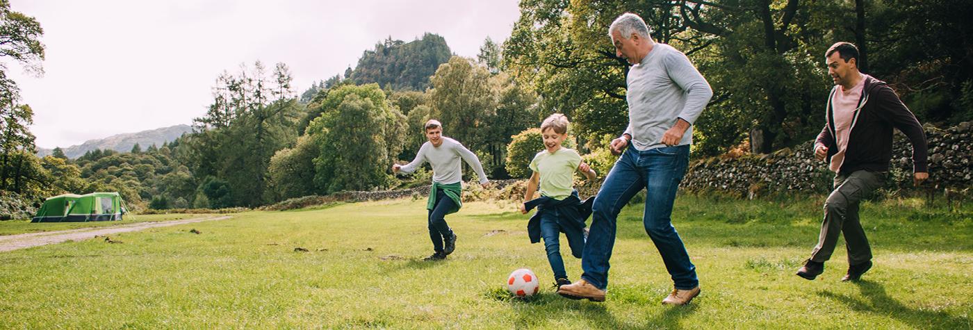 Three men and a young boy play soccer together in a park.