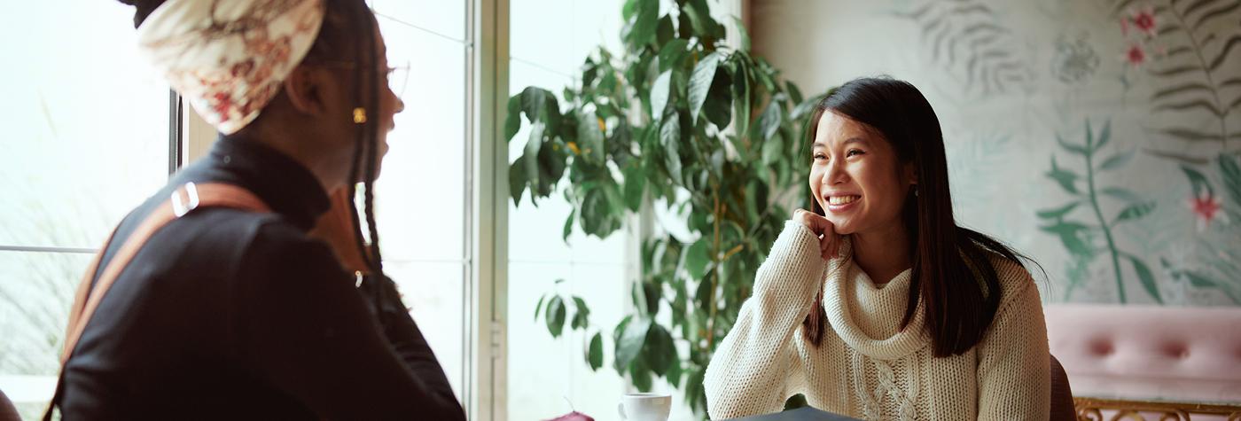 Two women speak with one another while seated at a restaurant table. 