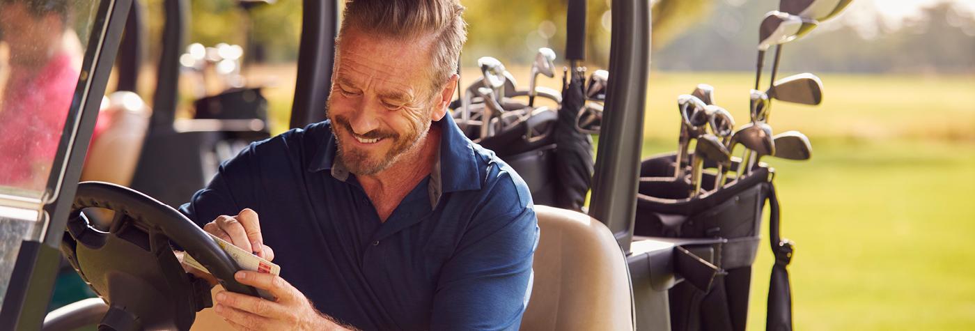 A man sits at the steering wheel of a golf cart as he fills out his scorecard. 