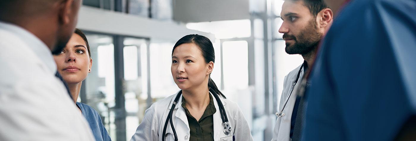 A diverse team of doctors stands in a common area and has a discussion.