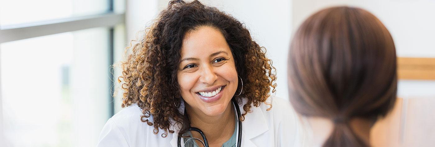 A smiling mid adult female doctor listens as a female patient discusses her health.