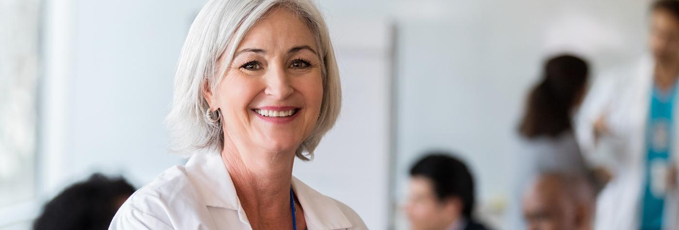 A woman in a white coat smiles at the camera.