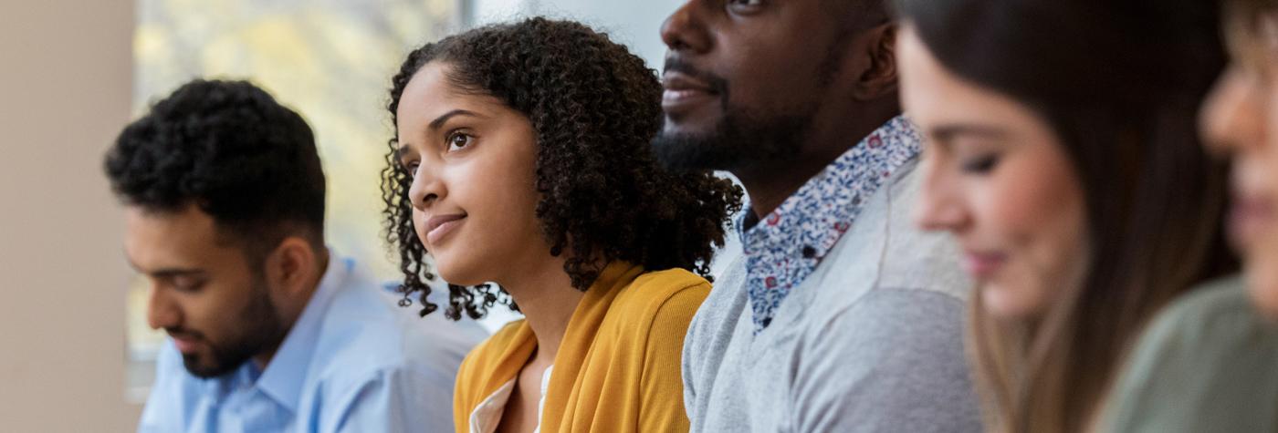 A diverse group of young adults sits side by side in a classroom. 