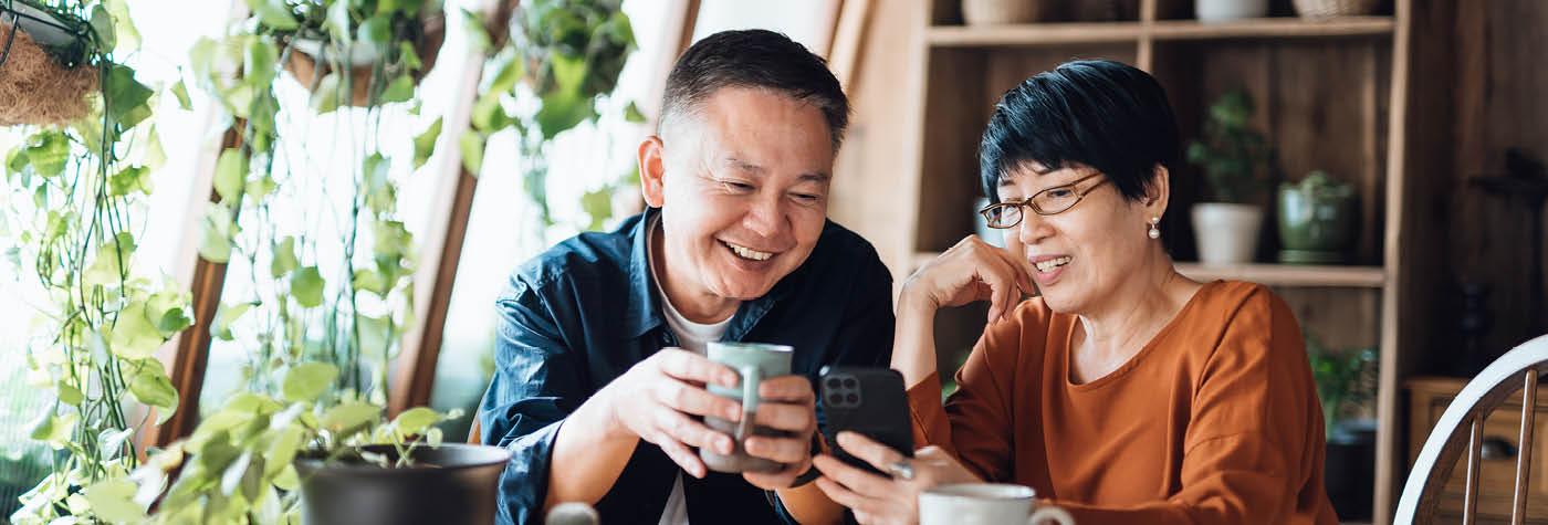 An Asian-American man and woman sit together while using a smart phone to video chat.