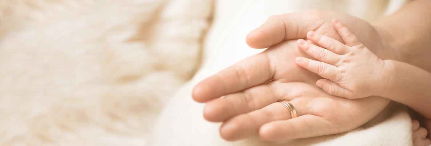 A baby's hand rests on his mother's hand.