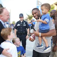 Coach Stoops and his two sons talk with Wesley Woodyard, a former UK linebacker, who is carrying a little boy in his arms.