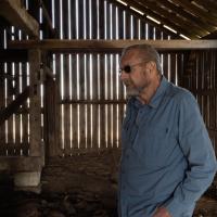 Howard Galbreath standing in a makeshift wooden shed on his farm.