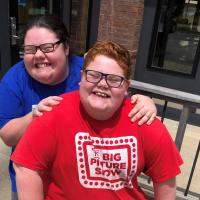 A photo of Abby standing behind Drew with her hands on his shoulders as they both smile for the camera.