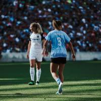 Arin looks across the field during a game with a full stadium. The back of her jersey is visible and her number is 3.