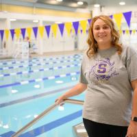 Callie stands next to a pool, smiling as she holds onto the handrail.