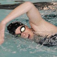 An action shot of Callie swimming. She is wearing a dark swimsuit, goggles, and a black swim cap.