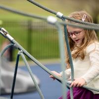 A candid photo of Cate walking across a rope bridge at a playground.