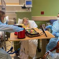 A photo of Cate sitting up in her hospital bed and laughing as her care team plays music for her.