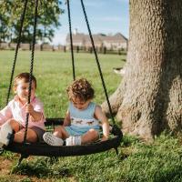 Charlie and his older brother, Baylor, sit on a netted swing in front of a tree. Both are smiling.