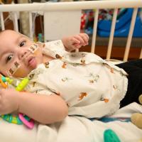 A close-up photo of a young patient looking into the camera as they lay in their bed.