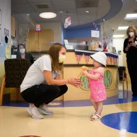 A candid photo of Sydney getting down on a patient’s level to hand them a toy, with Jennifer looking on in the background.