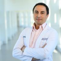 Dr. Alexandre Ancheta, a middle aged man with short black hair, stands in the hallway of UK HealthCare, wearing a white doctor’s coat and a pink shirt.