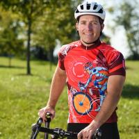 Dr. Stephen Duncan, a youthful-looking white man, smiles in a close-up portrait. He is outside, wearing a red cycling jersey and a white helmet.