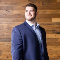 A portrait of Eli in a suit smiling as he looks off camera into the distance.