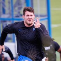 An action shot of Eli running during football training. His pinky finger is seen bandaged up.