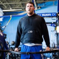 An action shot of Eli after completing a weight lifting rep. He has a determined look on his face.