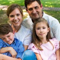 The Crittenden family poses for a group photo, sitting together on the grass. Elliott is smiling and scrunching his face into his mom’s arm.