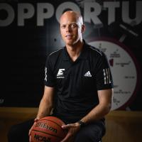 A.W. holds a basketball as he poses in front of a wall with a clock decal and line that reads “Opportunity.”