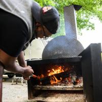 A candid photo of Joshua using a small shovel to stoke the flames of his smoker.