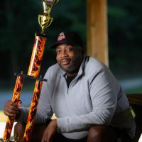 A photo of Joshua posing with the trophy he won from a barbecue competition.