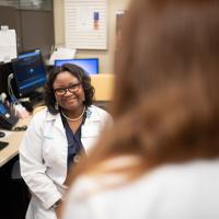 Joy smiles from behind a work station as someone talks to her.