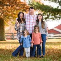 A photo of the Shaughnessy family posing together outside a fence and a red barn blurred in the background.