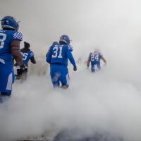 Kenneth makes an entrance onto the football field filled with smoke, alongside his football teammates.