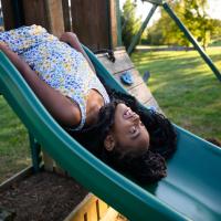 Kristen looks up to the sky and smiles as she lays upside down on top of the slide.