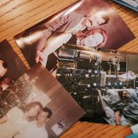 Four photographs are spread out on a table. Pictured in three of the photographs are Mae and her husband, Bobby, in their earlier years, posed in a warm embrace and standing close to one another. The fourth image is captured in a hospital room, with an individual attached to several machines, laying in a hospital bed.