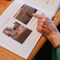 Mae is flipping through a photobook, pointing to a picture her grandchildren drew.