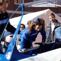 Luke Fortner, a young white man with a football player’s build, brown hair, and a brown beard, helps a young girl into the cart. She is wearing UK blue and has a bow in her hair.