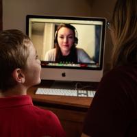 An over-the-shoulder shot of Max and Amy sitting in front of a computer. We can see a diabetes educator—a young brunette woman—on the screen.