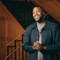 A photo of Michael clasping his hands together as he smiles and looks off camera.
