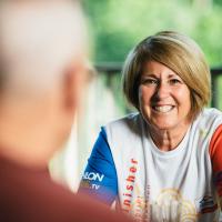 Patty smiles across a table at her husband on their porch.