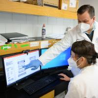 Dr. D’Orazio points to something on the Dr. Hong Pu’s computer screen. Dr. Hong Pu is an older Asian woman with medium-length graying hair pulled back in a bun. She is glasses and a white lab coat over a white shirt.