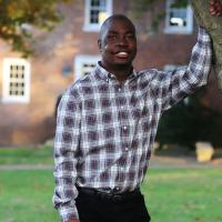 With one hand holding the branch of a tree, Remilson looks towards the camera and smiles.