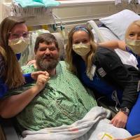 A photo of Ronald and a team of his nurses smiling for the photo from the side of his hospital bed.